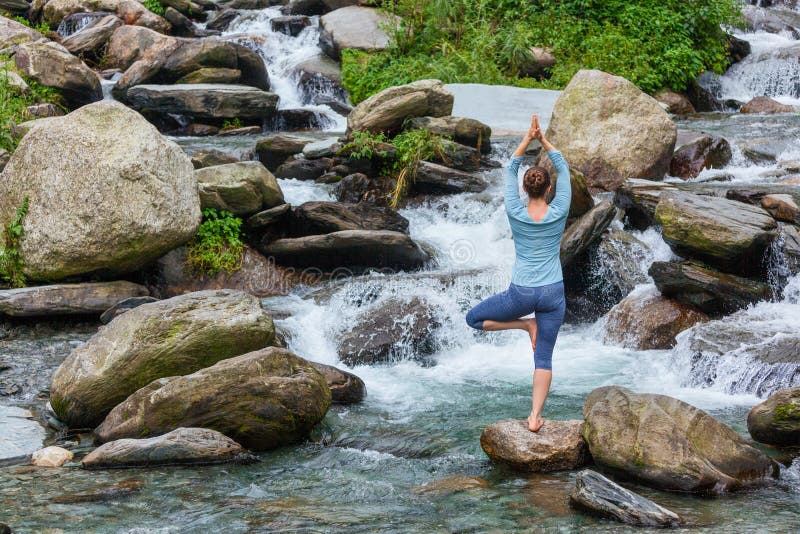De vrouw in de boom van Vrikshasana van yogaasana stelt in openlucht bij waterval stock afbeelding De vrouw in de boom van Vrikshasana van yogaasana stelt in openlucht bij waterval stock afbeelding
