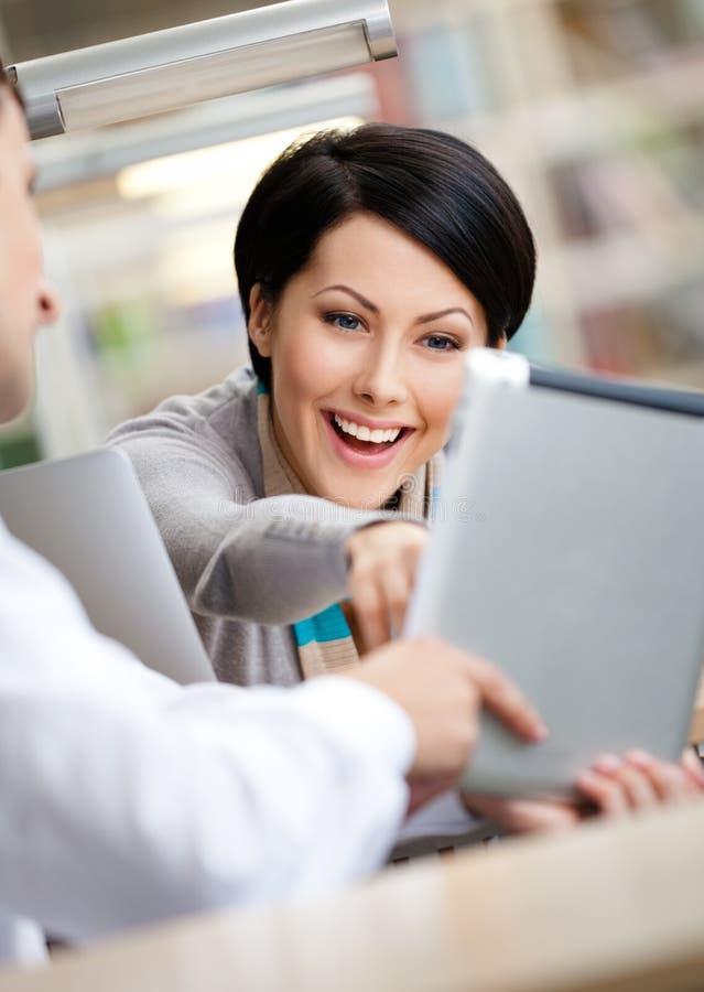 Woman communicates with men showing her something in the pad sitting at the table at the library. Woman communicates with men showing her something in the pad sitting at the table at the library