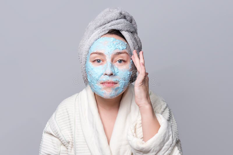 Woman applying facial clay mask at spa salon or at home, skincare theme. Face mask, spa beauty treatment with copy space on gray background. Woman applying facial clay mask at spa salon or at home, skincare theme. Face mask, spa beauty treatment with copy space on gray background