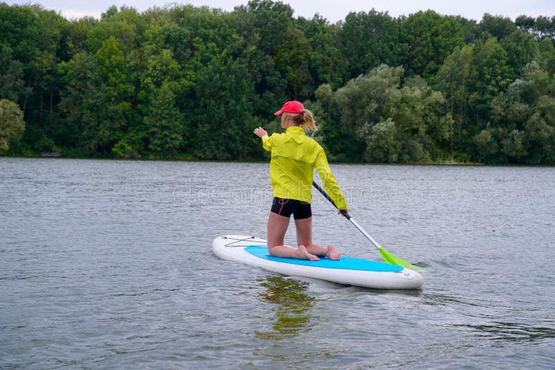 De vrouw knielt op een surfplank en houdt een peddel Achtermeningsfoto stock foto's De vrouw knielt op een surfplank en houdt een peddel Achtermeningsfoto stock foto's