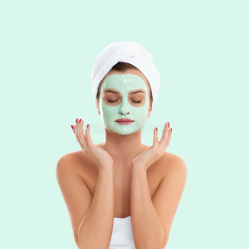 Beautiful woman is getting facial clay mask on pastel green background. Beauty, cosmetics, body care and spa concept. Beautiful woman is getting facial clay mask on pastel green background. Beauty, cosmetics, body care and spa concept