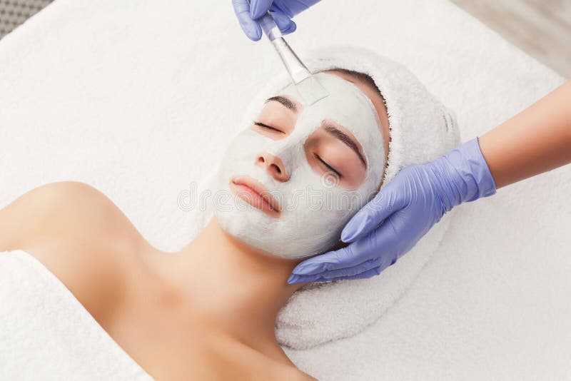 Face peeling mask, spa beauty treatment, skincare. Woman getting facial care by beautician at spa salon, side view, close-up. Face peeling mask, spa beauty treatment, skincare. Woman getting facial care by beautician at spa salon, side view, close-up