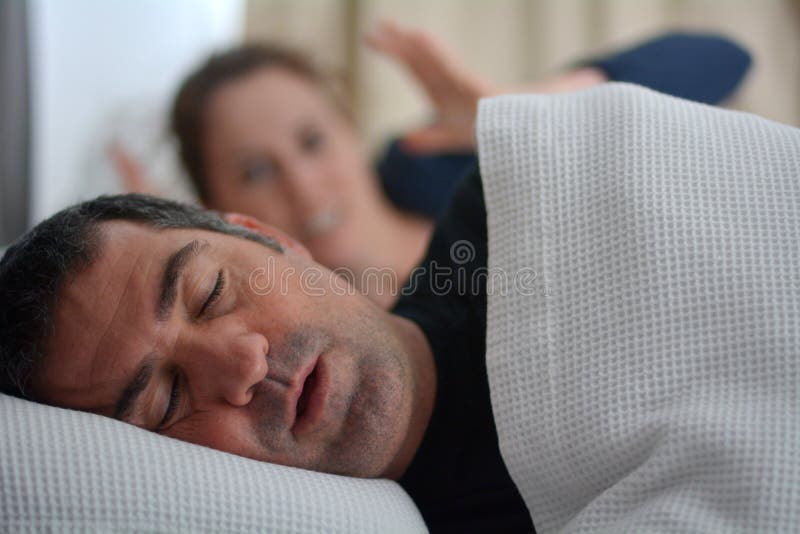De vrouw lijdt aan haar mannelijke partner snurkend in bed stock afbeelding De vrouw lijdt aan haar mannelijke partner snurkend in bed stock afbeelding