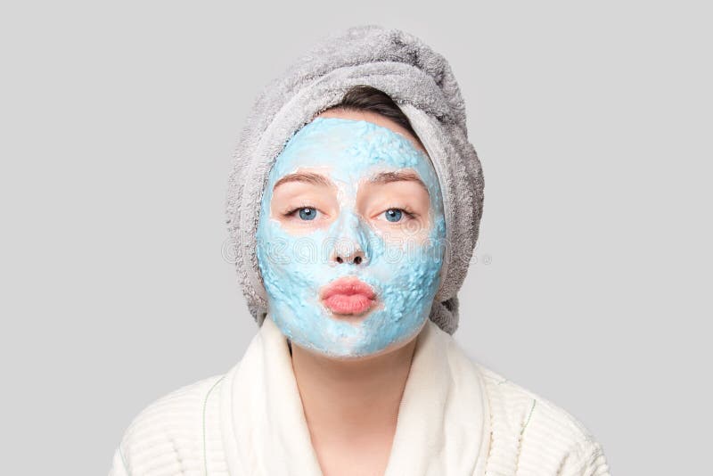 Woman with facial clay mask at spa salon or at home, skincare theme. Girl removes alginate cosmetic mask. Face mask, spa beauty treatment with copy space on gray background. Woman with facial clay mask at spa salon or at home, skincare theme. Girl removes alginate cosmetic mask. Face mask, spa beauty treatment with copy space on gray background