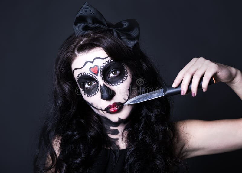De vrouw met Halloween-schedel maakt omhoog het snijden van haar gezicht met mes o stock foto De vrouw met Halloween-schedel maakt omhoog het snijden van haar gezicht met mes o stock foto