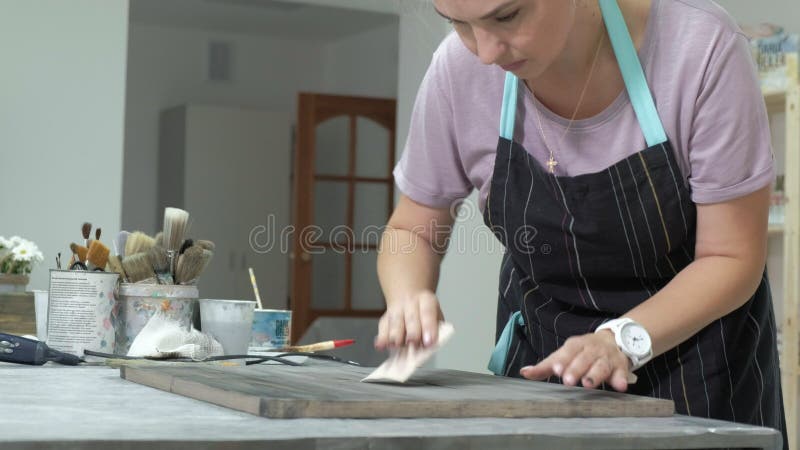 De vrouw in de workshop werkt aan houten raad, die een effect van antiquiteit creëren