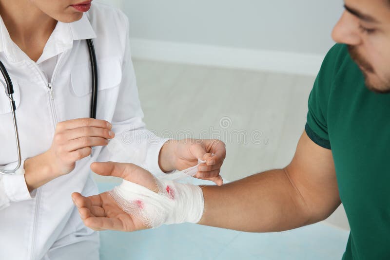 De vrouwelijke arts die verband op jonge man toepassen dient kliniek in Eerste hulp royalty-vrije stock foto's De vrouwelijke arts die verband op jonge man toepassen dient kliniek in Eerste hulp royalty-vrije stock foto's