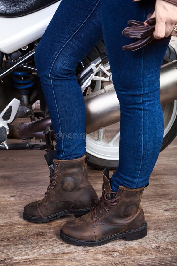 De vrouwelijke benen die jeans en de bruine laarzen van de leerveiligheid voor motorrijden dragen zijn dichtbij motor, sluiten om stock foto's De vrouwelijke benen die jeans en de bruine laarzen van de leerveiligheid voor motorrijden dragen zijn dichtbij motor, sluiten om stock foto's
