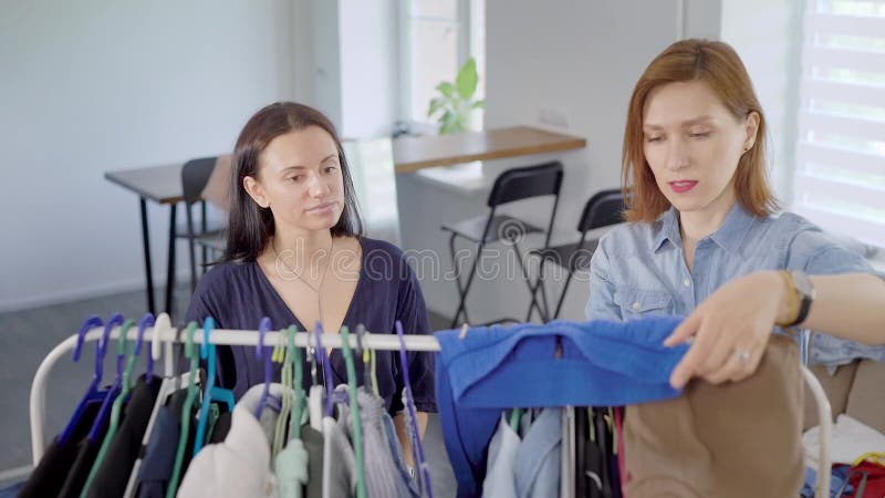 De vrouwen bestuderen kleren op een hanger worden gehangen die Kiezen van een garderobe is zeer belangrijk voor moderne vrouwen