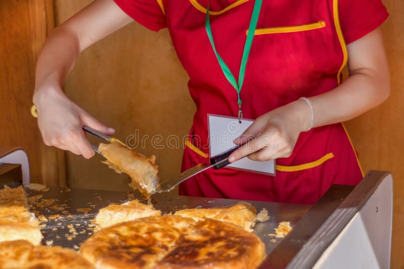 De vrouwenarbeider snijdt een Balkan burek met kaas in bakkerijwinkel stock fotografie De vrouwenarbeider snijdt een Balkan burek met kaas in bakkerijwinkel stock fotografie