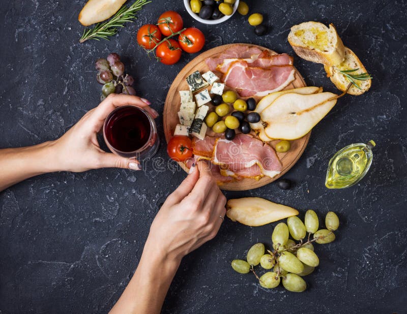 De vrouwenhanden houden een glas wijn Voorgerecht, Italiaanse antipasto, ham, olijven, kaas, brood, druiven, peer op donkere stee royalty-vrije stock foto De vrouwenhanden houden een glas wijn Voorgerecht, Italiaanse antipasto, ham, olijven, kaas, brood, druiven, peer op donkere stee royalty-vrije stock foto