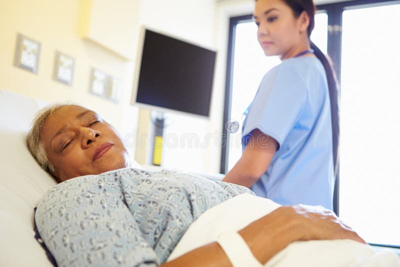 Nurse Watching Sleeping Senior Woman Patient In Hospital Room Wearing Scrubs. Nurse Watching Sleeping Senior Woman Patient In Hospital Room Wearing Scrubs