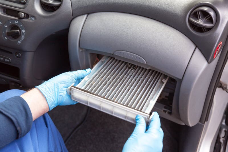 A technician, sitting in a car, replacing old and dirty cabin air filter while wearing protective workwear and gloves. A technician, sitting in a car, replacing old and dirty cabin air filter while wearing protective workwear and gloves.