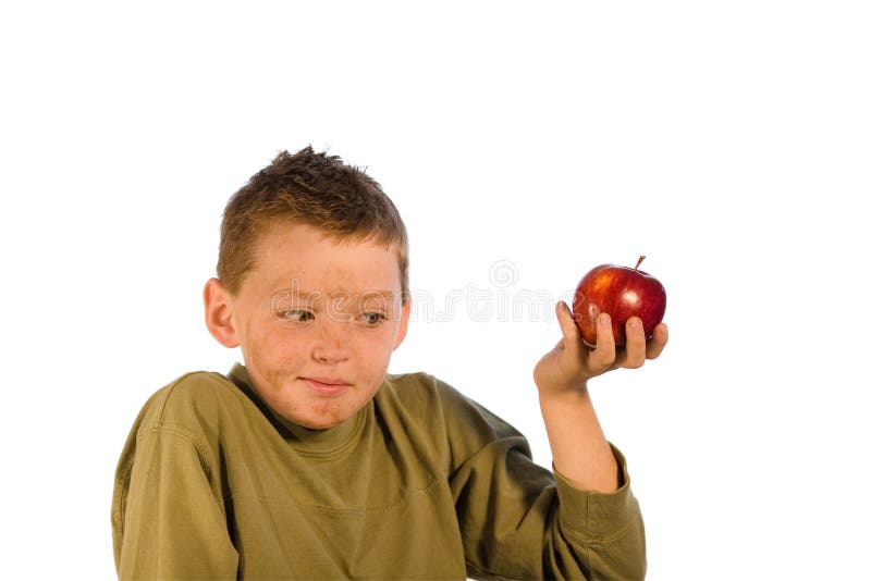 Very dirty young boy holding an apple and looking embarrased. Studio shot isolated on a white background. Very dirty young boy holding an apple and looking embarrased. Studio shot isolated on a white background.