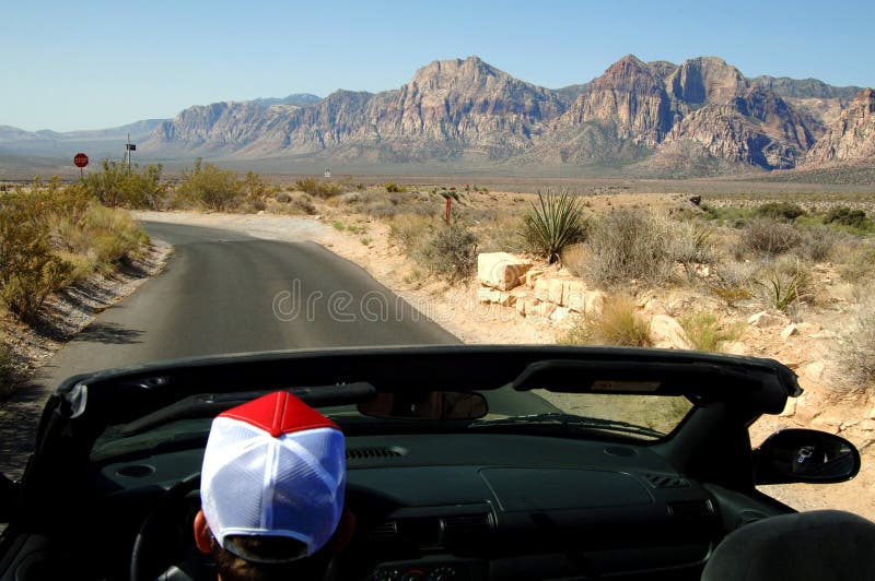 A man driving in a convertible on the road leading to the mountains. A man driving in a convertible on the road leading to the mountains