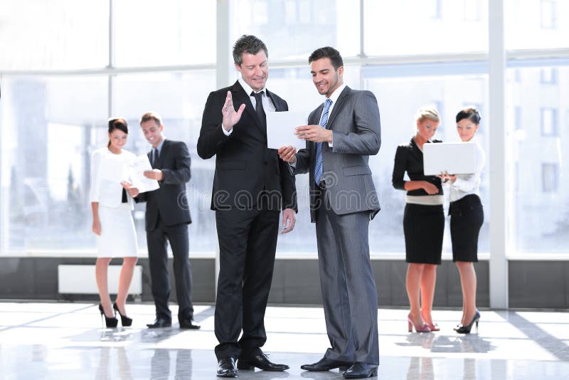 De werknemers bespreken discussienota die zich in de hal van het bureau bevinden stock afbeelding De werknemers bespreken discussienota die zich in de hal van het bureau bevinden stock afbeelding