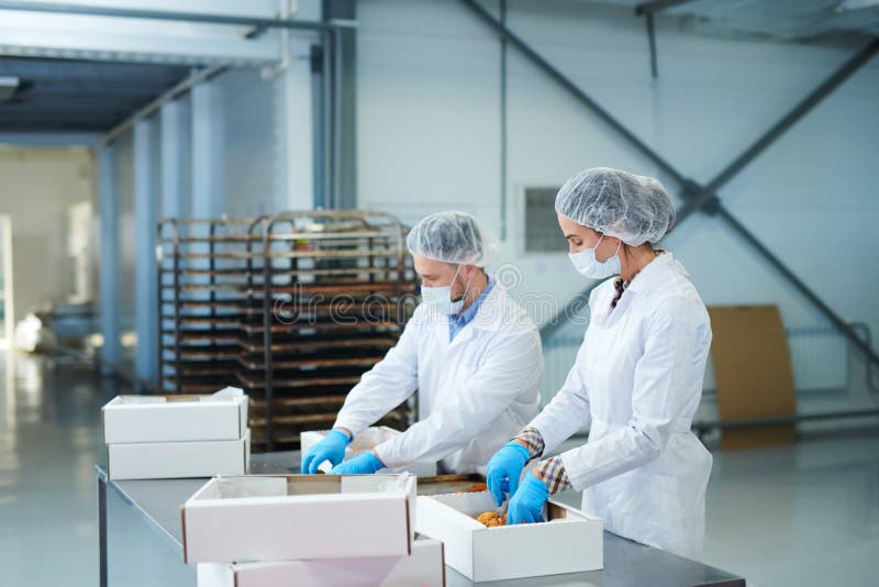 De werknemers die van de banketbakkerijfabriek gebakje inpakken in dozen