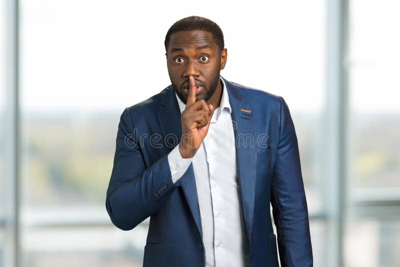 Businessman holding index finger on lips. Black man showing silence gesture with finger on his lips. Sign keep a silence. Businessman holding index finger on lips. Black man showing silence gesture with finger on his lips. Sign keep a silence.