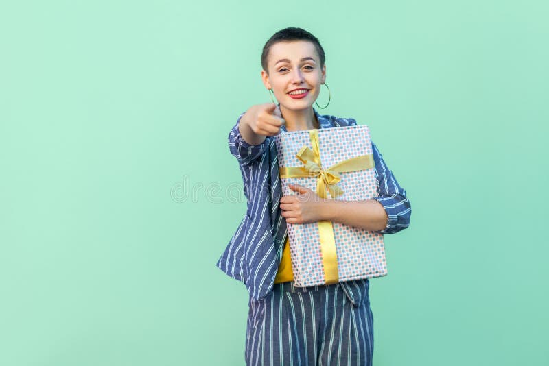 De winnaar is u! Portret van gelukkige mooi met korte haar jonge vrouw in gestreept, huidige doos koesteren en kostuum die richte stock afbeelding De winnaar is u! Portret van gelukkige mooi met korte haar jonge vrouw in gestreept, huidige doos koesteren en kostuum die richte stock afbeelding