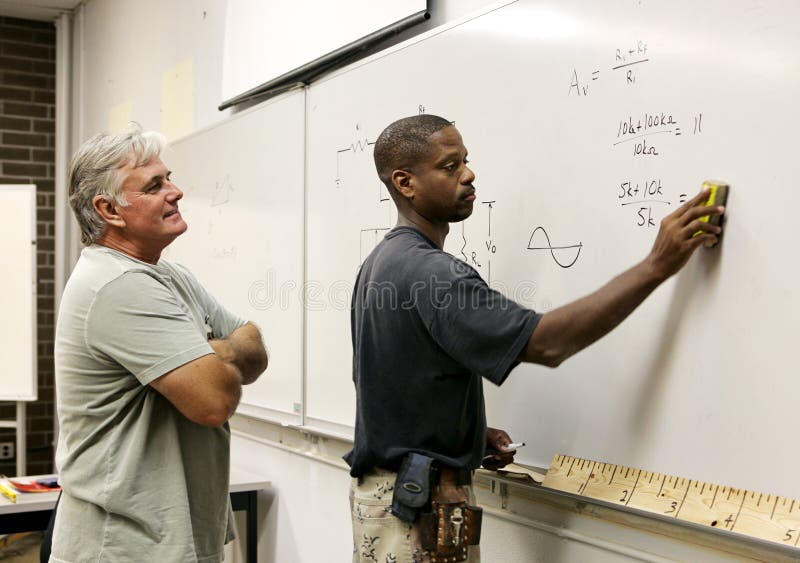 A teacher looks on as his adult education student erases the board. A teacher looks on as his adult education student erases the board.