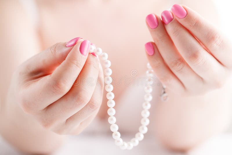 De witte parels in vrouwelijke handen, met spijkers schilderden roze royalty-vrije stock afbeeldingen De witte parels in vrouwelijke handen, met spijkers schilderden roze royalty-vrije stock afbeeldingen
