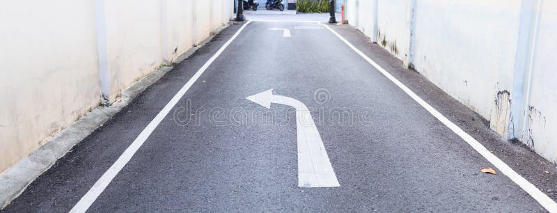 De witte pijlverkeersteken wijzen op minder belangrijke te draaien weg weggegaan om weg en witte voetpadlijnen op de asfalt lande stock fotografie De witte pijlverkeersteken wijzen op minder belangrijke te draaien weg weggegaan om weg en witte voetpadlijnen op de asfalt lande stock fotografie