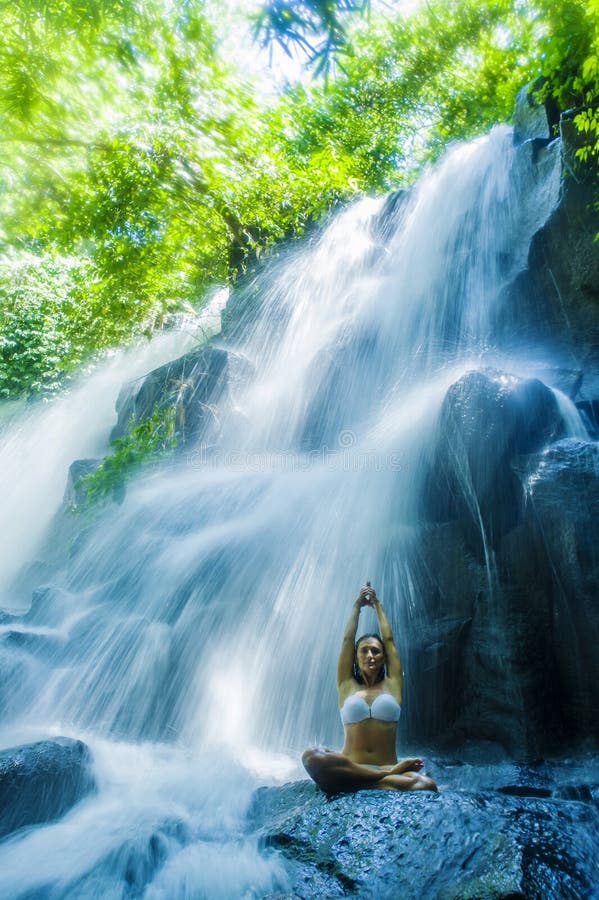De yoga van de vrouwenzitting stelt in geestelijke ontspanningssereniteit en meditatie bij het overweldigen van mooi waterval en stock foto De yoga van de vrouwenzitting stelt in geestelijke ontspanningssereniteit en meditatie bij het overweldigen van mooi waterval en stock foto