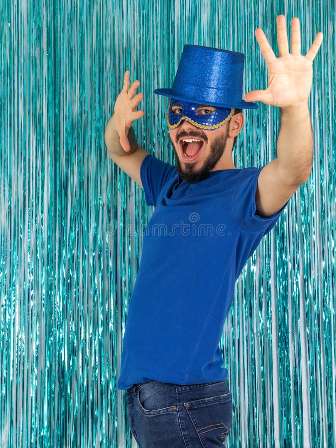 Bearded man is shouting and with his hands raised. Brazilian is wearing blue clothes: top hat and mask. Carnival, Mardi Gras, New Year`s Eve. Style, mystery. Bearded man is shouting and with his hands raised. Brazilian is wearing blue clothes: top hat and mask. Carnival, Mardi Gras, New Year`s Eve. Style, mystery.