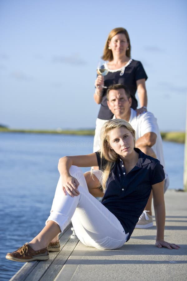 De zitting van de tiener op dok door water met ouders stock foto De zitting van de tiener op dok door water met ouders stock foto