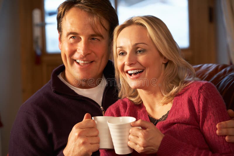 Middle Aged Couple Sitting On Sofa With Hot Drinks Watching TV. Middle Aged Couple Sitting On Sofa With Hot Drinks Watching TV