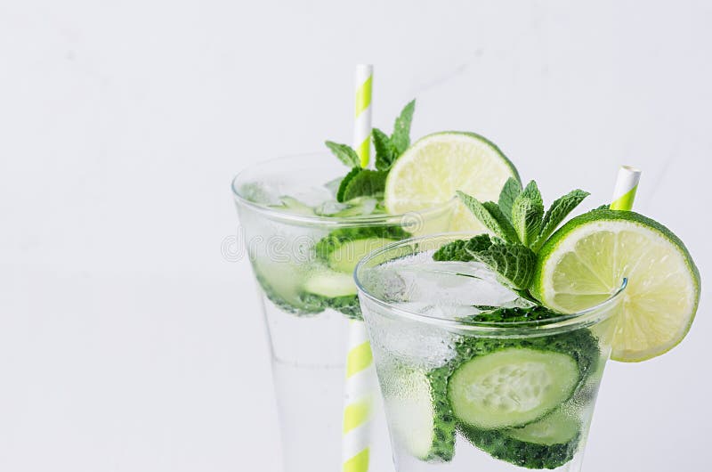 De zomer koude transparante drank met ijsblokjes, plakkenkalk, komkommer, stro en takjesmunt op witte houten raad, close-up royalty-vrije stock afbeeldingen De zomer koude transparante drank met ijsblokjes, plakkenkalk, komkommer, stro en takjesmunt op witte houten raad, close-up royalty-vrije stock afbeeldingen