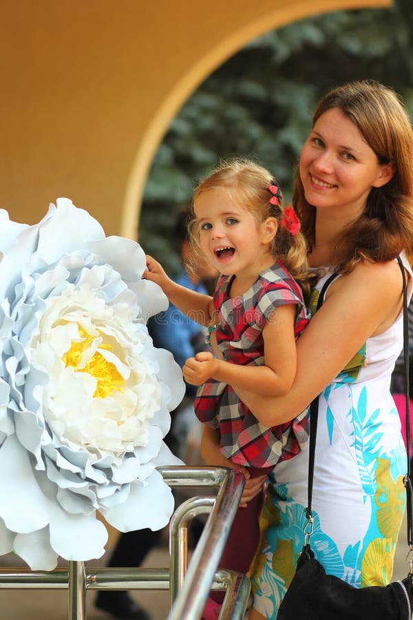 De zomerportret van een gelukkige glimlachende moeder en een dochter in feestelijke kleren met bloemen stock afbeelding De zomerportret van een gelukkige glimlachende moeder en een dochter in feestelijke kleren met bloemen stock afbeelding