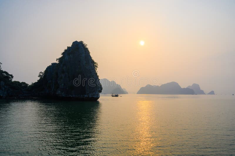 De zonsondergang in Ha snakt Baai, Vietnam Zonsondergang achter nevelige rotsvormingen, boot in voorgrond, bezinningen in Overzee royalty-vrije stock foto De zonsondergang in Ha snakt Baai, Vietnam Zonsondergang achter nevelige rotsvormingen, boot in voorgrond, bezinningen in Overzee royalty-vrije stock foto