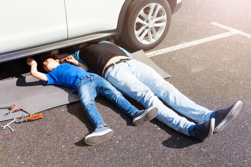 De zoon van het vaderonderwijs aan reparatieauto die onder auto liggen royalty-vrije stock foto's De zoon van het vaderonderwijs aan reparatieauto die onder auto liggen royalty-vrije stock foto's