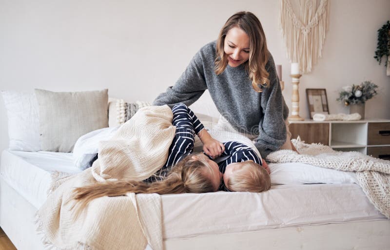 De zorg van de moeder Jonge moeder die kinderen omvatten met een deken in slaapkamer Broer en zuster die en op het bed omhelzen s stock fotografie De zorg van de moeder Jonge moeder die kinderen omvatten met een deken in slaapkamer Broer en zuster die en op het bed omhelzen s stock fotografie