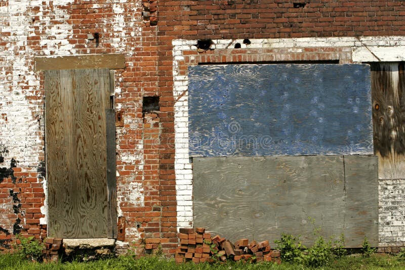 Detail of old, abandoned brick factory wall with chipped and peeling paint. Copy space on boarded up door or blue and grey boarded up window. Detail of old, abandoned brick factory wall with chipped and peeling paint. Copy space on boarded up door or blue and grey boarded up window.