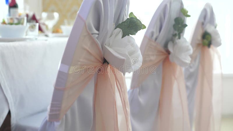 Decor with white roses and pink ribbons on empty white chairs in preparation for the wedding ceremony. Colorful