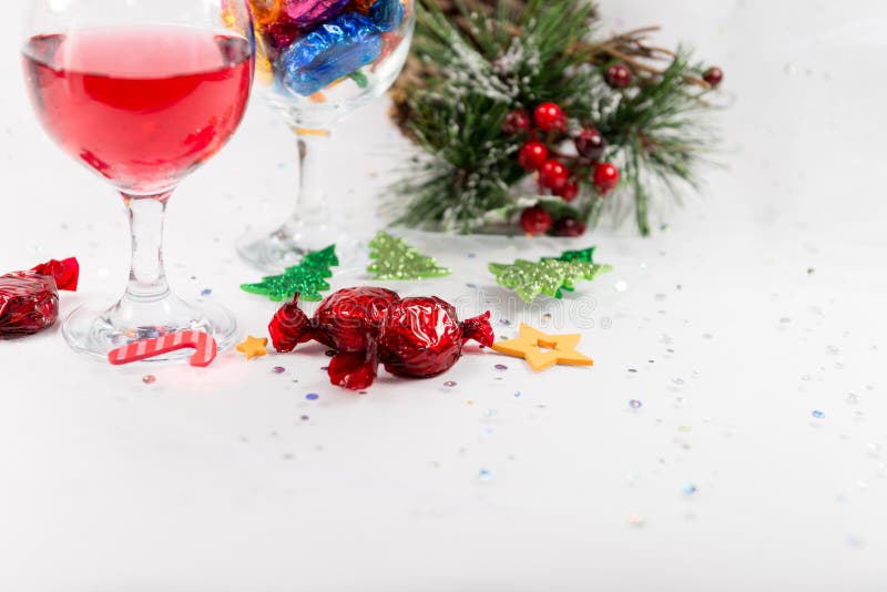 Close up of Christmas party table decorations with wine and wrapped chocolate candy sweets. Treats to enjoy the merry holiday season. On a snowy white background. Copy space. Close up of Christmas party table decorations with wine and wrapped chocolate candy sweets. Treats to enjoy the merry holiday season. On a snowy white background. Copy space