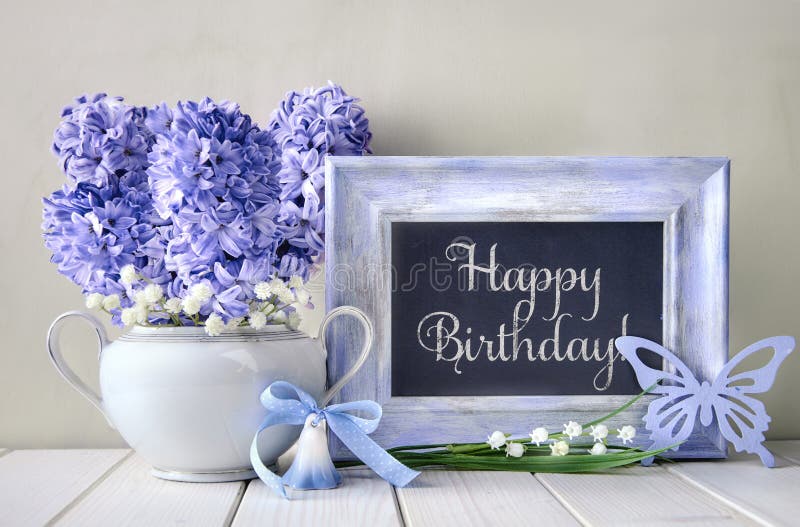Decoración azul y flores de jacinto sobre mesa blanca, pizarra con texto \'Feliz cumpleaños.