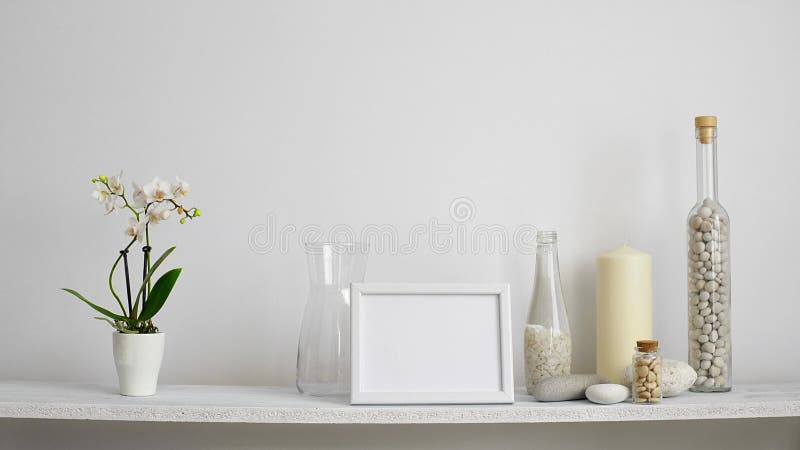 Decoración moderna del sitio con la maqueta del marco Estante contra la pared blanca con la vela, el vidrio y las rocas decorati