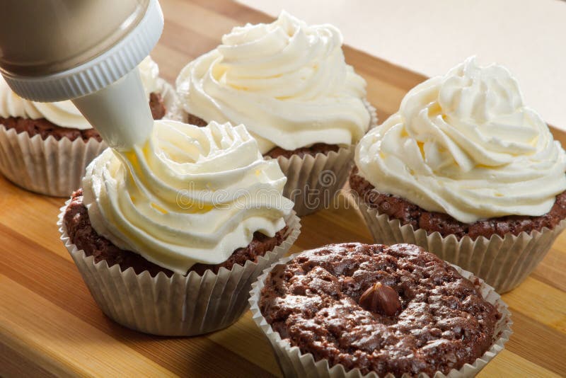 Decorating chocolate muffin with vanilla cream on wooden board. Decorating chocolate muffin with vanilla cream on wooden board