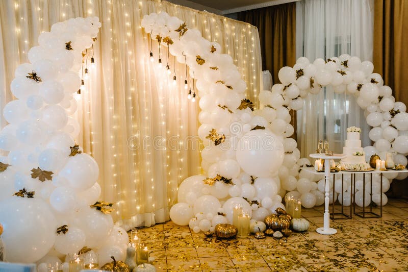 Decorated arch for wedding ceremony. White balloons, candles, autumn leaves and small pumpkins. Autumn location and Halloween decor.