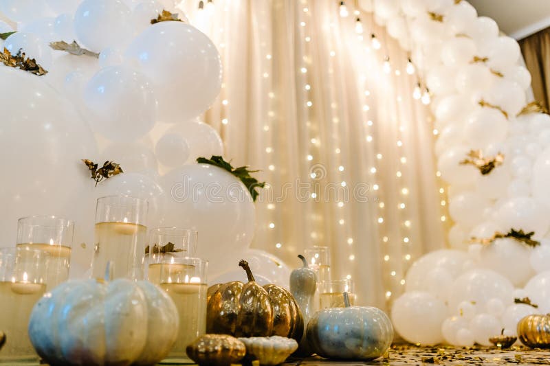 Decorated arch for wedding ceremony. White balloons, candles, autumn leaves and small pumpkins. Autumn location and Halloween decor.