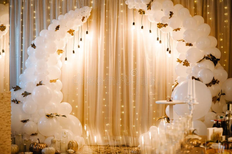 Decorated arch for the wedding ceremony. White balloons, candles, autumn leaves and small pumpkins. Autumn location and Halloween decor.