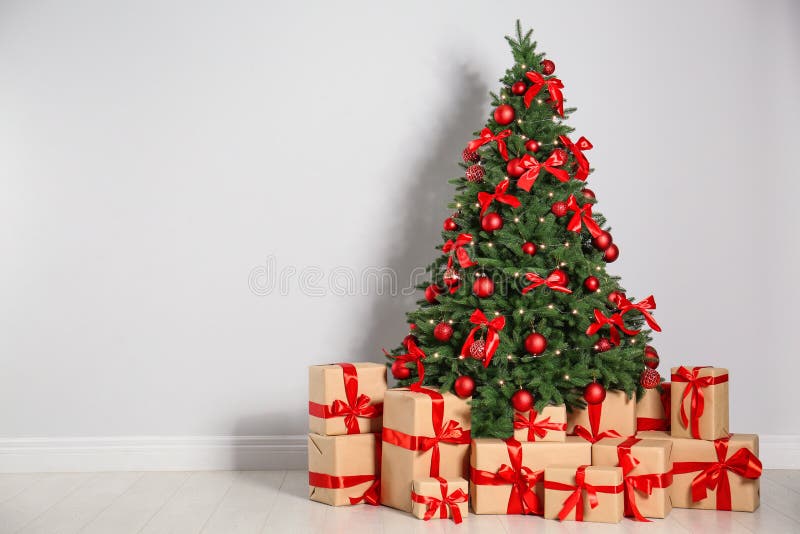 Decorated Christmas tree and gift boxes near light wall
