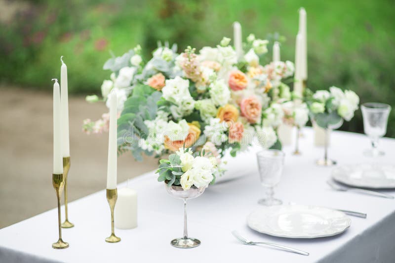 Decorated wedding table for two with beautiful flower composition, glasses for wine, candles and plates, outdoor, fine