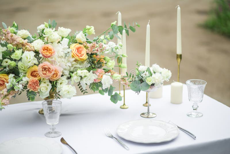 Decorated wedding table for two with beautiful flower composition, glasses for wine, candles and plates, outdoor, fine