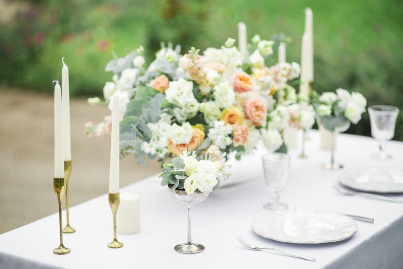 Decorated wedding table for two with beautiful flower composition, glasses for wine, candles and plates, outdoor, fine