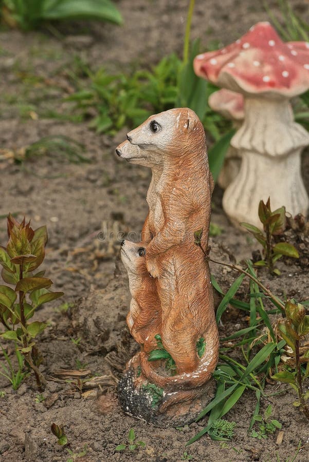 Decorative ceramic sculpture toy of three brown gophers stands on gray ground in a summer garden among green vegetation