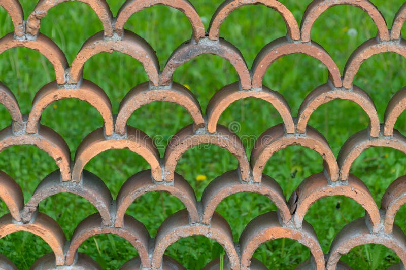 Decorative fence made of semicircular bricks, arranged in a staggered pattern, creating a unique design with gaps between the stock photo